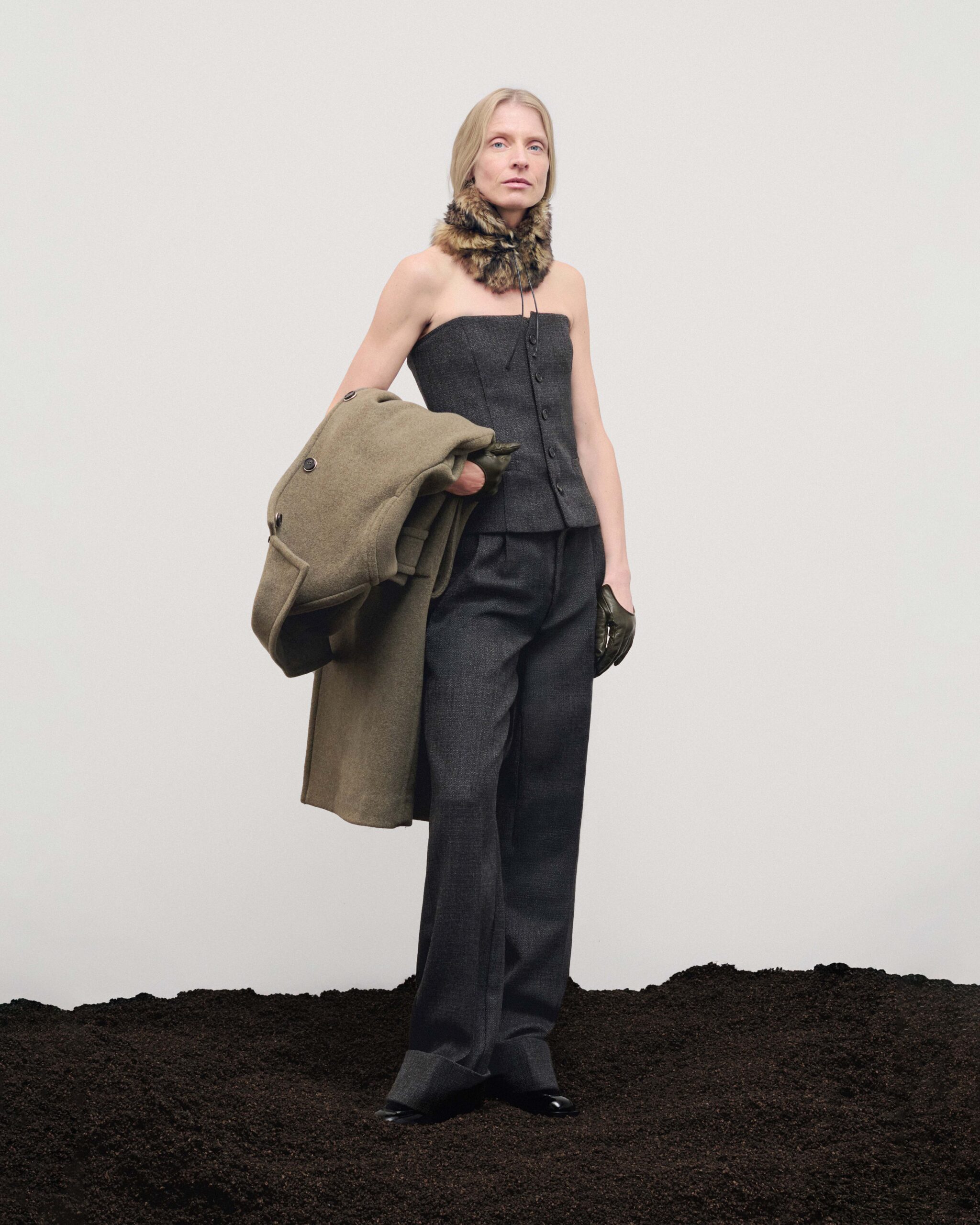 Strapless wool bustier with wide trousers, khaki coat carried over the arm and forest green leather gloves, Durazzi Milano FW26