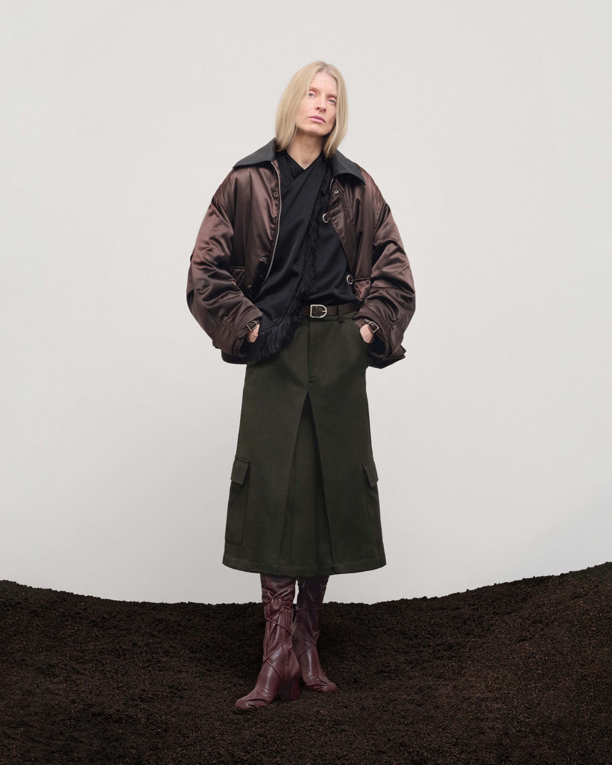 Brown satin bomber with black leather collar over olive cargo midi skirt, brown leather belt and boots, Durazzi Milano FW26