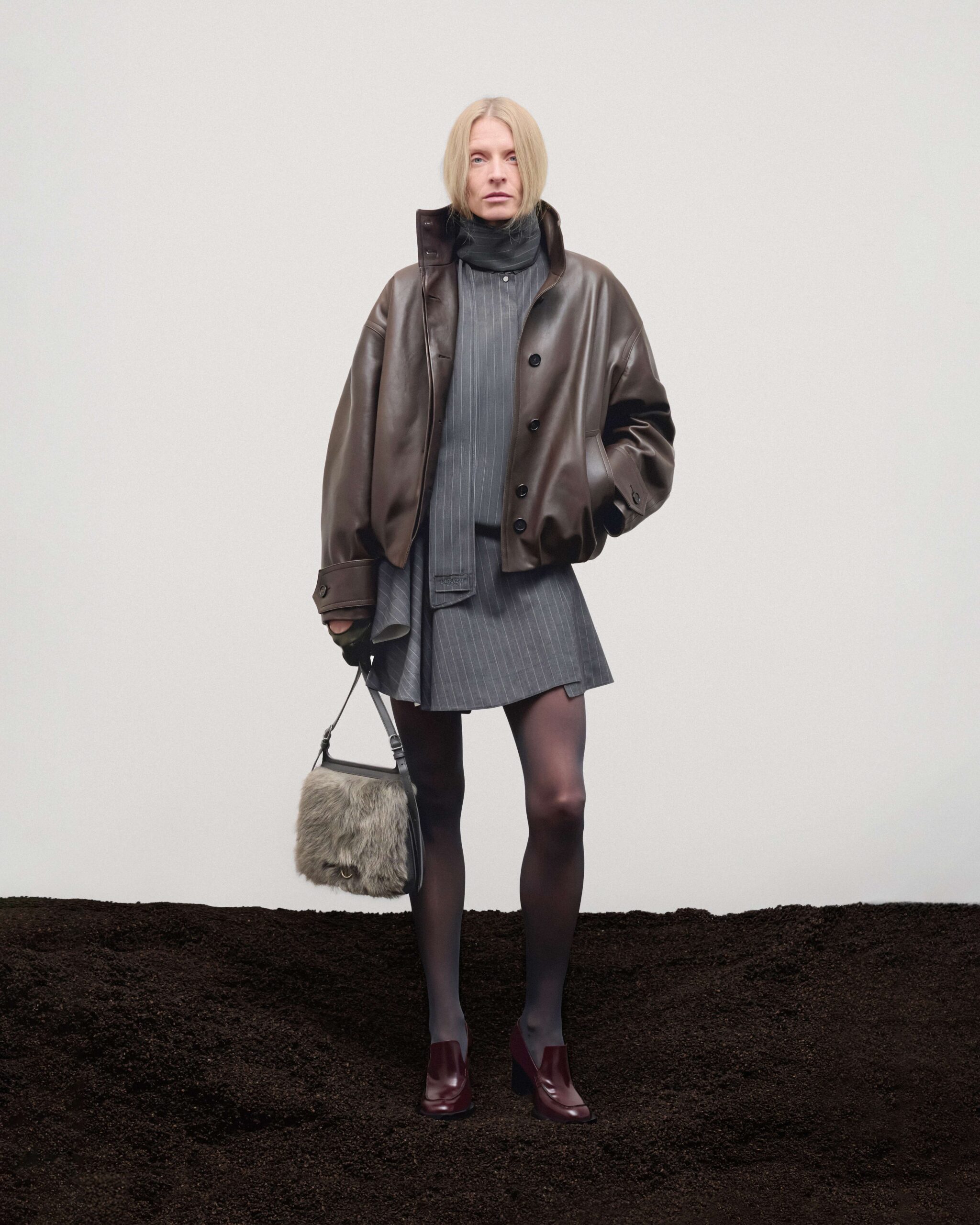 Brown leather bomber over pinstripe mini dress with removable foulard, leather and shearling bag and burgundy leather heeled loafers, Durazzi Milano FW26