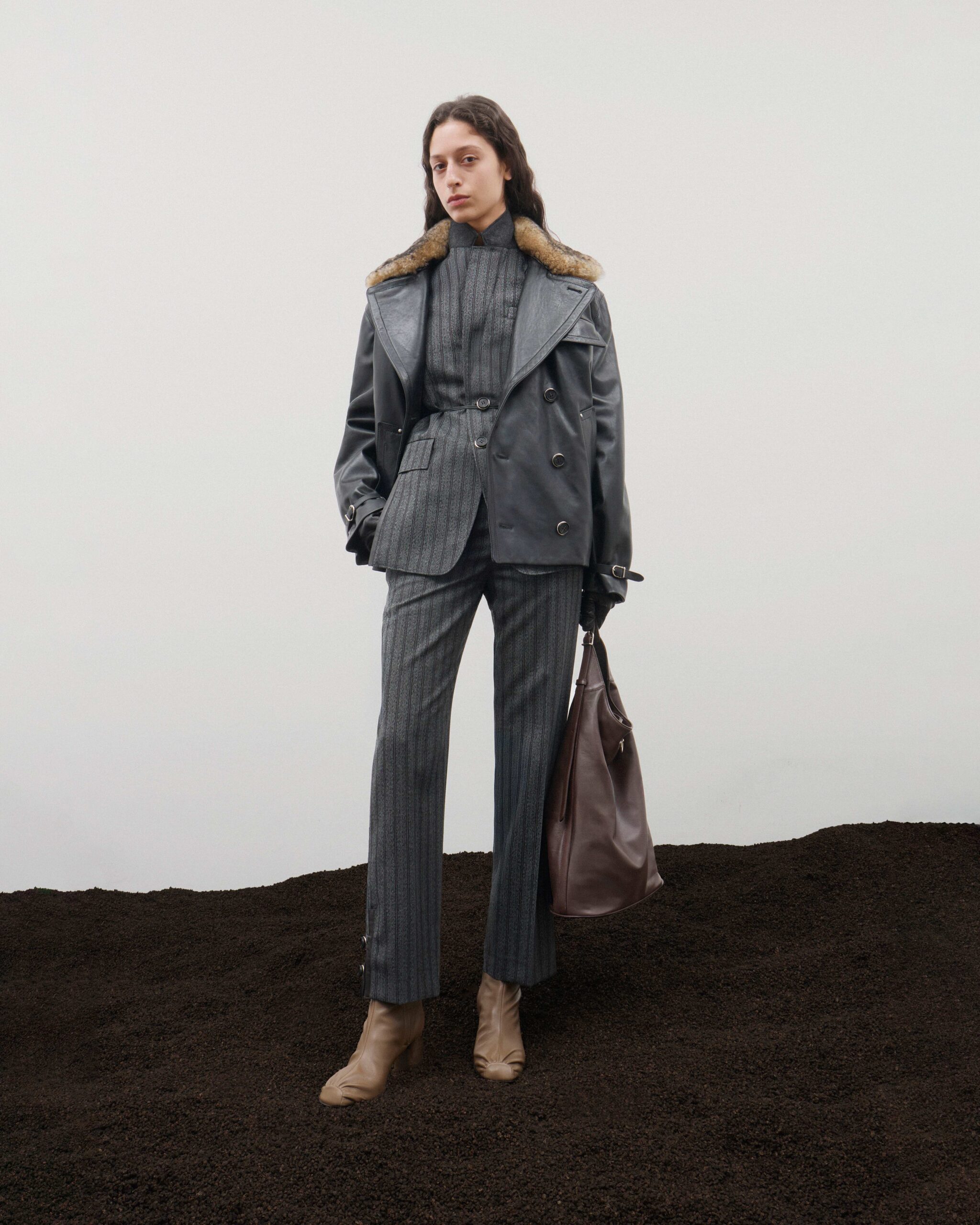 Grey leather coat with fur collar over pinstripe suit, burgundy leather tote, Durazzi Milano FW26