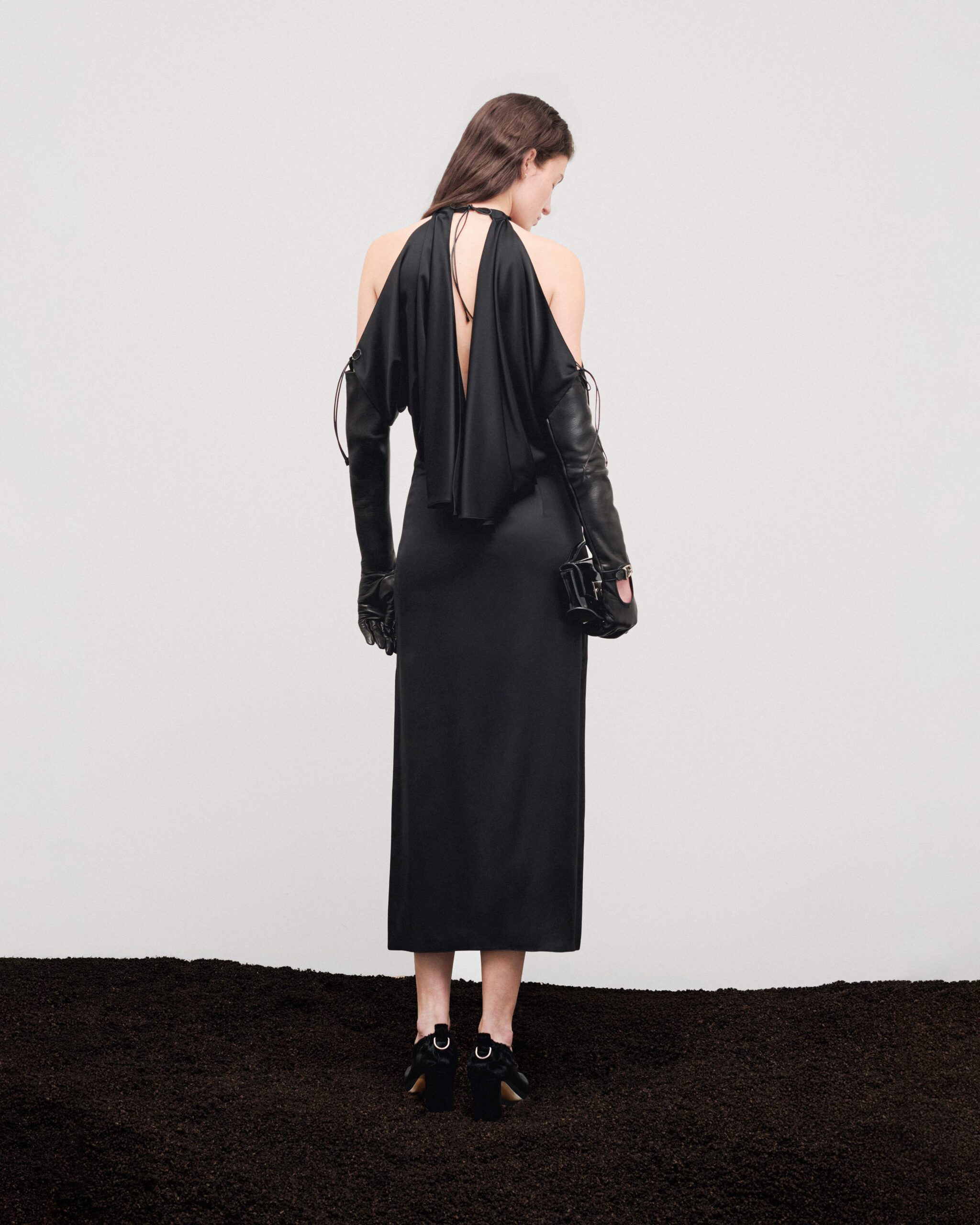 Open-back draped silk long dress with long leather gloves, black patent leather Mini Swing bag and black leather heels, rear view, Durazzi Milano FW26